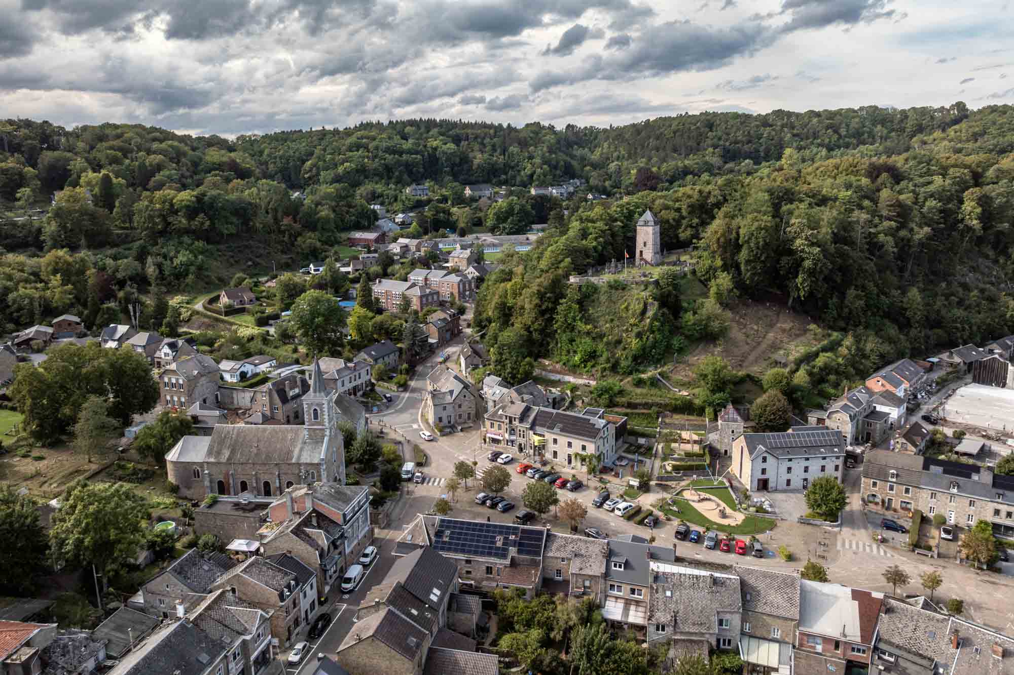 Vue aérienne du village de Comblain-au-Pont au cœur d’une vallée boisée.