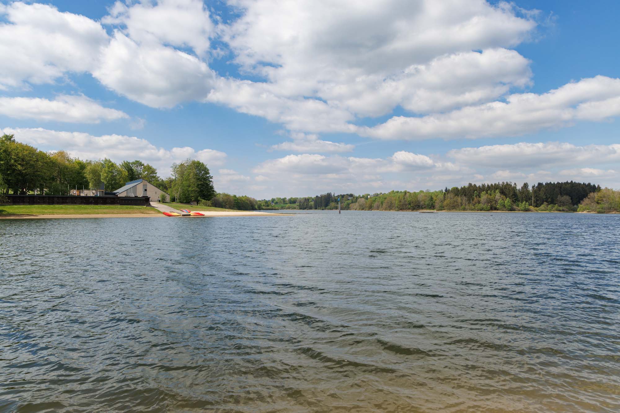 Meer van Bütgenbach met strand en bos onder een licht bewolkte hemel